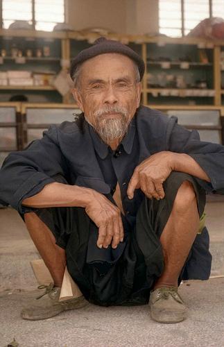 Old man squatting on steps; Market at Menghum, Menghai District, Xishuangbanna Region, Yunnan, China